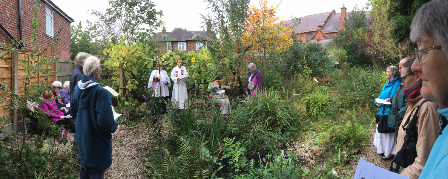 Panoramic photo of blessing of wildlife garden including priest in robes and members of congregation